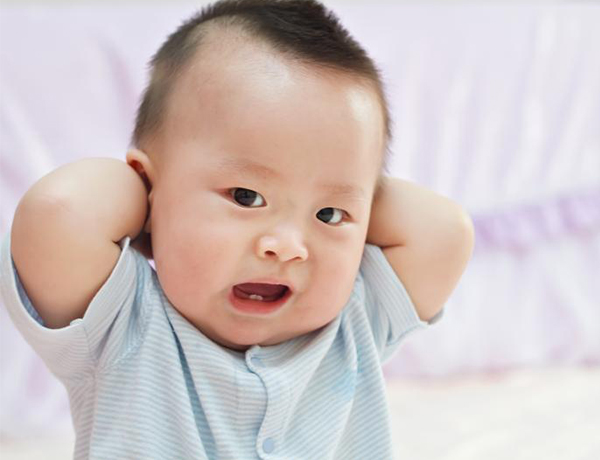 An Asian baby boy with his hands behind his head.