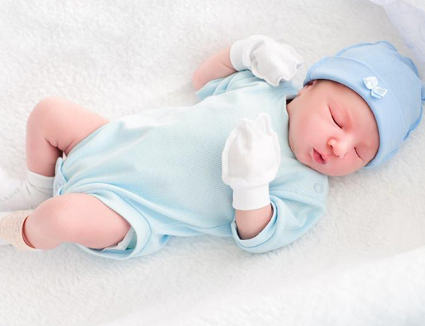 A newborn baby sleeps on a white blanket.
