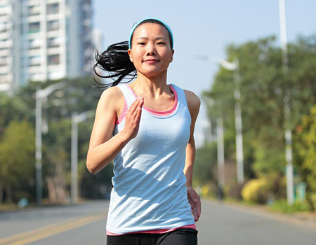 A young asian woman in sports wear runs in to the middle of an empty city road.