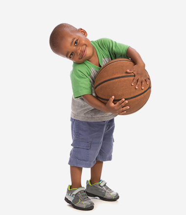 A young boy tilts his head and smiles while hugging a basketball.