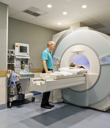 A medical professional activates the motorized bed of a Magnetic Resonance Imaging (MRI) scanner to begin a study of a female patient.