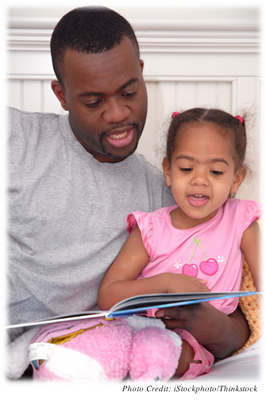 A young girl around 4 or 5 years old reading with her father