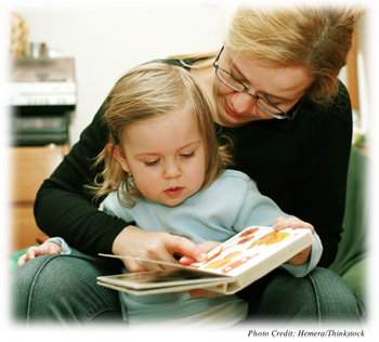 A young girl around 2 or 3 years old looking at a book with a woman