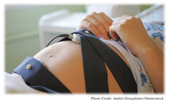 A pregnant woman with two Doppler devices gently strapped around her at the top and bottom of her pregnant belly 