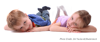 A young boy and girl lying on their stomachs smiling and looking at the camera
