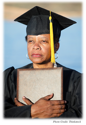 A middle-aged woman in a cap and gown holding a diploma