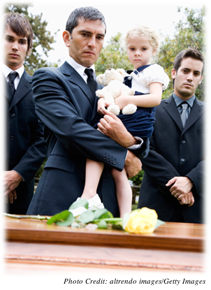 Three men dressed in dark suits staring at a coffin with a single yellow  rose on top of it.  One is holding a young girl with her teddy bear.