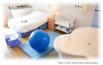 A hospital birth room that contains a tub, a mat, a comfortable bed, and a big, inflated ball which are all items that serve to make a mother who is going through labor more comfortable.