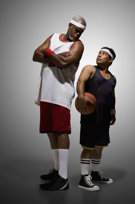 Two men dressed as basketball players stand beside each other. One man is much taller than the other man.