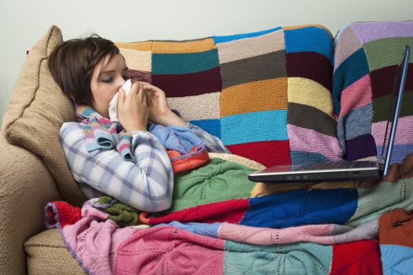 A young woman has the flu and looks at a laptop, probably to understand flu predictions made online. 