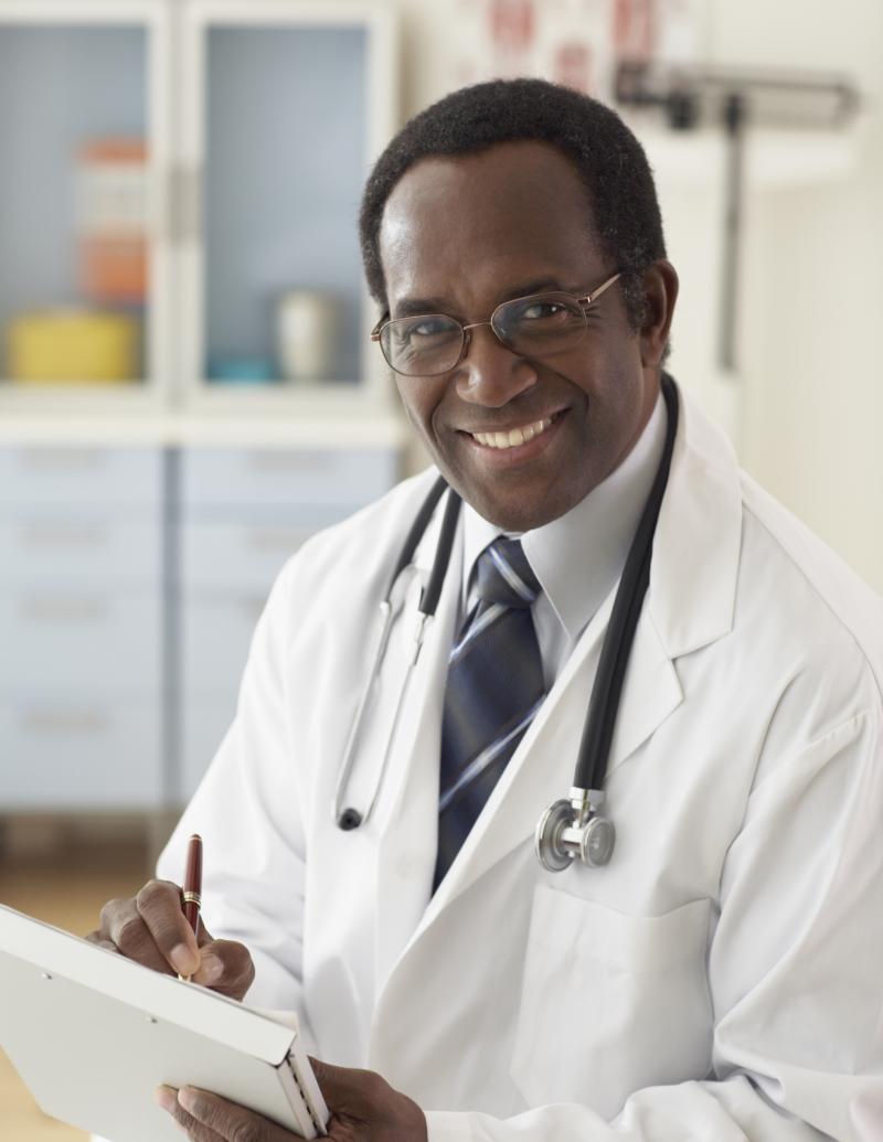 photo of a smiling, male, nonwhite medical doctor holding a clipboard or some charts/folders.] 