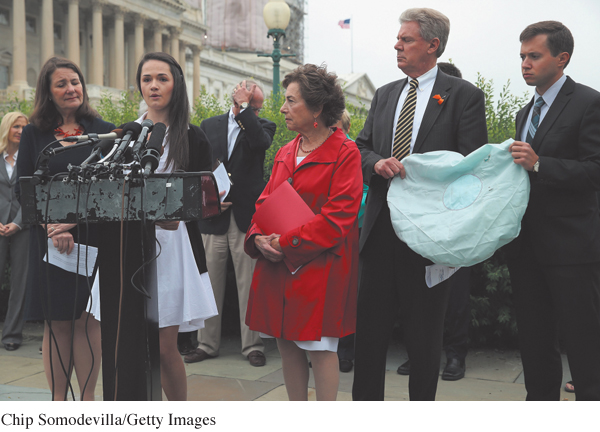 An image shows Angelina Sujata speaking in front of the mike as she recalls her experience of being injured by Takata airbag. She is accompanied by few people by her side and at the background.
