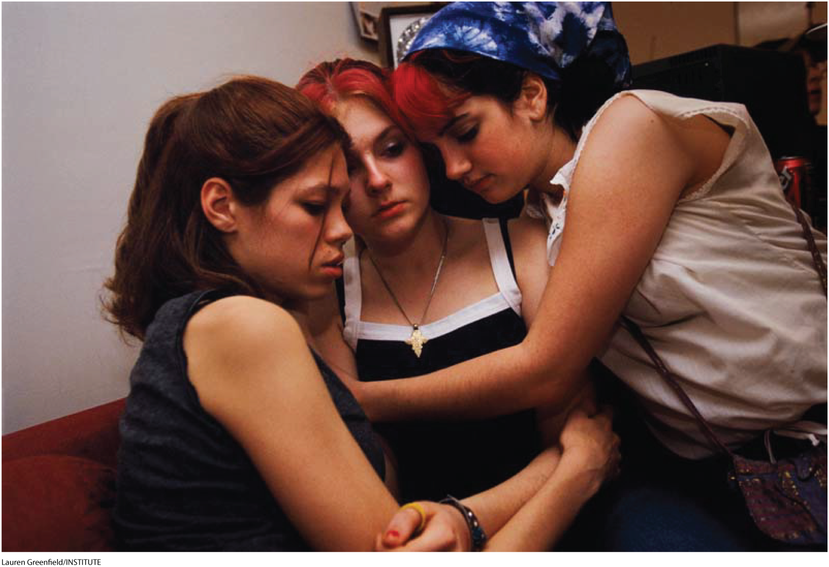 A photo shows three solemn looking teenage girls hugging each other. 