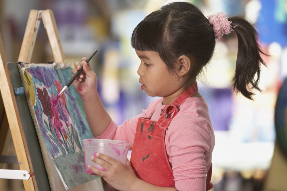 Young Asian girl painting at easel.
