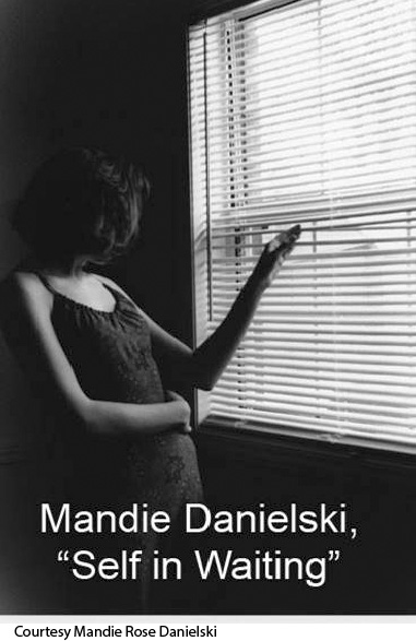 Black-and-white photo of a woman peeking through window blinds. The photographer’s name, Mandie Danielski, appears at the bottom with the title, Self in Waiting. 