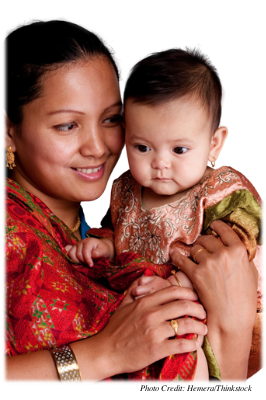 A smiling mother holding her baby who is gazing at something off-camera.