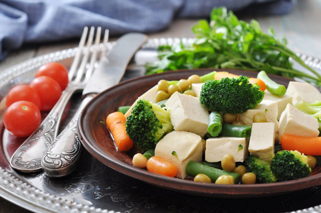 Tofu with boiled vegetables on plate and tomato closeup